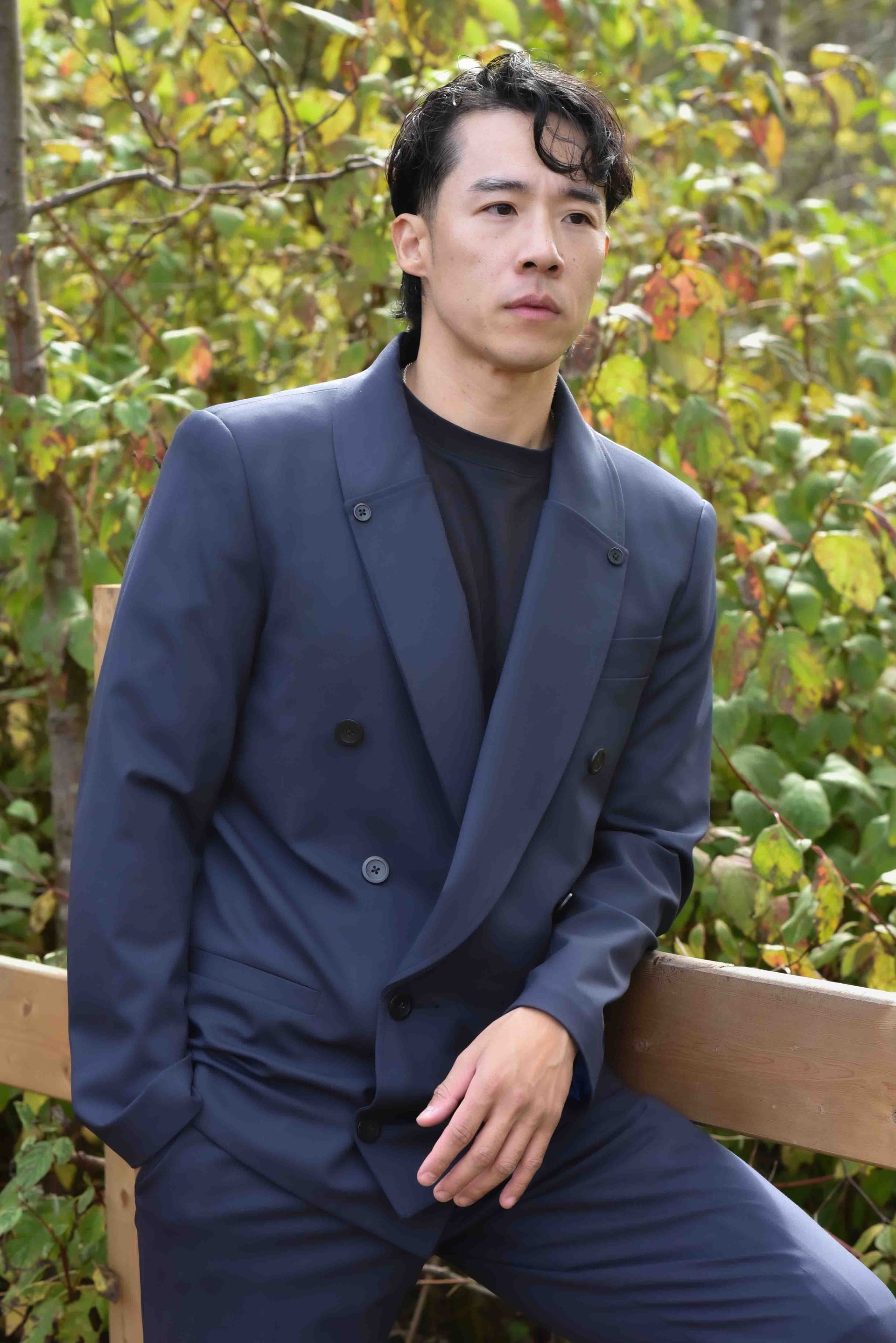 Man Wearing Zenith Blazer Shawl Collar and leaning over a wood fence in a forest background